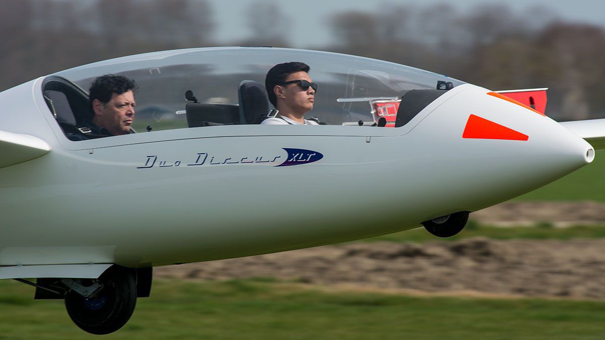 Instructeur en leerling samen in de cockpit van de Duo Discus, vlak boven het veld